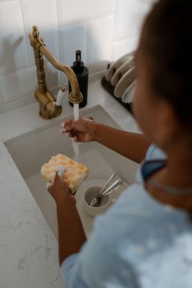 Child at the kitchen sink with a soapy sponge doing their dish washing chores.